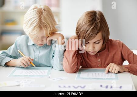 School children making notes on paper while sitting at the table during lesson Stock Photo
