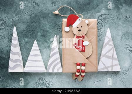Gift in craft paper on a green background, Christmas tree toy in the form of a bear with a heart in its paws with the inscription x-mas, triangular Stock Photo