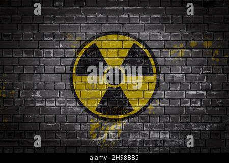 A shabby radiation sign depicted on a dark brick wall warning of radiation hazards Stock Photo