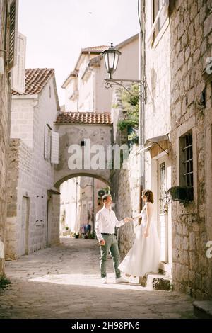 Bride and groom stand on a narrow cobbled street between old houses Stock Photo