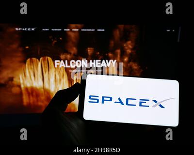 Person holding mobile phone with logo of company Space Exploration Technologies (SpaceX) on screen in front of web page. Focus on phone display. Stock Photo