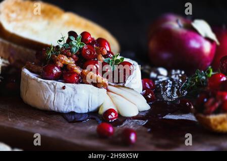 Baked Camembert Brie cheese with a cranberry, honey, balsamic vinegar and nut relish and garnished with thyme. Served with toasted bread slices and ap Stock Photo