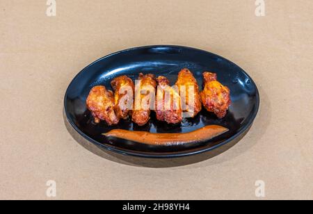 A closeup of spicy chicken wings on a black plate Stock Photo