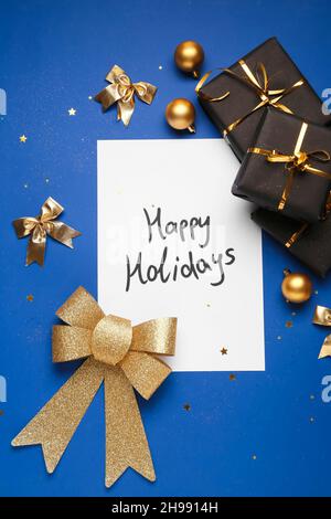 Greeting card with text HAPPY HOLIDAYS, Christmas decor and gift boxes on blue background Stock Photo