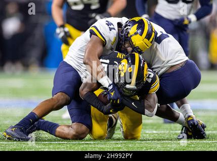 Indianapolis, Indiana, USA. 04th Dec, 2021. Michigan defenders Nikhai Hill-Green (41) and Brad Hawkins (2) makes the tackle on Iowa running back Tyler Goodson (15) during NCAA Football game action between the Michigan Wolverines and the Iowa Hawkeyes at Lucas Oil Stadium in Indianapolis, Indiana. Michigan defeated Iowa 42-3. John Mersits/CSM/Alamy Live News Stock Photo