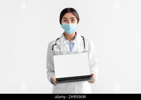 Millennial hindu woman in coat show laptop with empty screen, isolated on white background Stock Photo