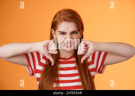 Displeased unhappy redhead female viewer frowning disappointed, give bad feedback watch awful movie, show thumbs-down hateful grimace, complain bad Stock Photo
