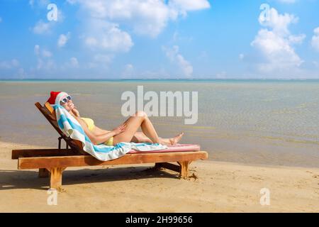 young woman in santa hat and sunglasses relaxing on sun lounger Stock Photo