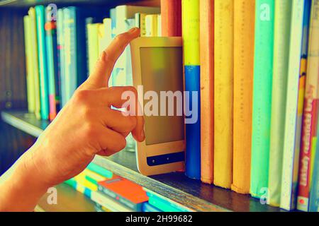 Electronic book picked from a library shelf. The electronic book on a bookshelf among the many books in the library. Booksand library concept. Stock Photo