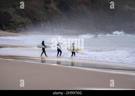 Three surfers enter the water for some surfing at the ever popular Praa Sands beach on the south coast of Cornwall. Stock Photo