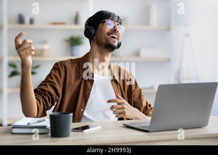 Happy indian guy with headset sitting at workdesk, singing Stock Photo