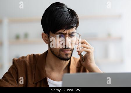 Concentrated indian manager working on laptop, having phone conversation Stock Photo