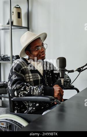 Vertical portrait of person in wheelchair giving interview while recording podcast in studio Stock Photo