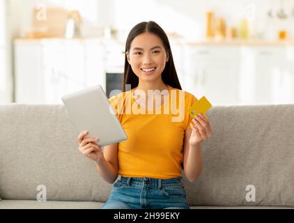 E-commerce and online purchases concept. Excited korean woman shopping on internet with tablet credit card Stock Photo