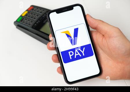 V Pay debit electronic payment system. A man pays for goods and services using a mobile application, smartphone and POS payment terminal. November 2021, San Francisco, USA Stock Photo