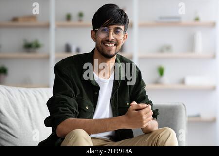 Positive middle eastern guy sitting on couch at home Stock Photo