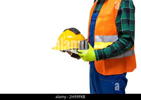Construction worker wearing work clothes and reflective vest, standing slightly sideways and holding a yellow helmet in his hands with headphones prot Stock Photo