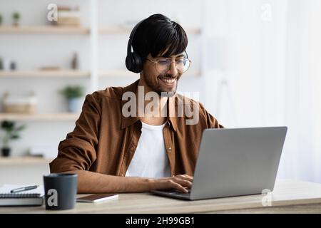 Smiling indian guy attending webinar, typing on laptop keyboard Stock Photo