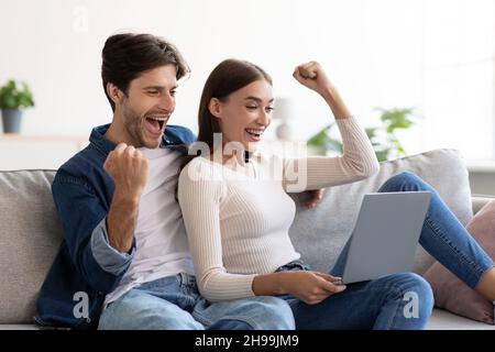 Happy smiling excited young european male and woman celebrating victory in online game on laptop Stock Photo