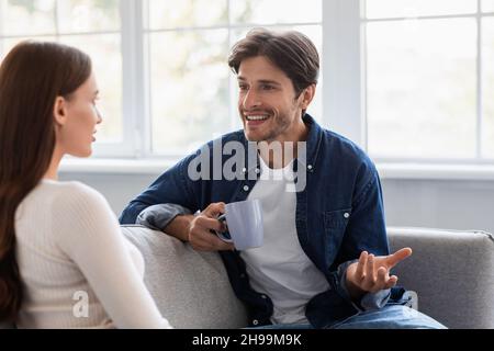 Smiling young caucasian man and woman with cups of coffee, talk and spending weekend together Stock Photo