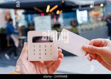 Crop anonymous female client with plastic card making contactless NFC payment on terminal for order in outdoors cafe in city Stock Photo
