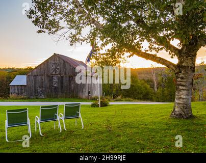rustic gray barn back lit by the setting sun on a country road Stock Photo