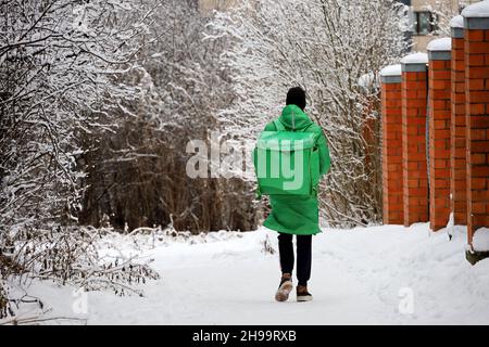 Delivery service courier with a thermos bag walking down the snow in winter city. Food delivery home Stock Photo