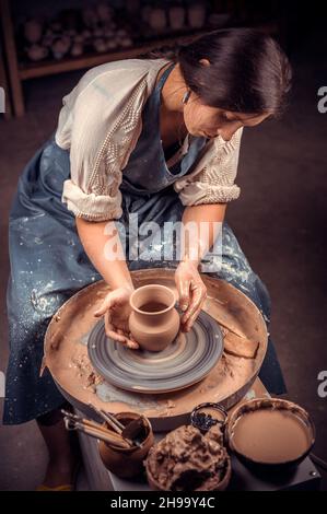 Beautiful young woman master demonstrates the process of making ceramic dishes using the old technology. Handwork. Stock Photo