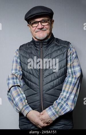 a senior man in a down vest with glasses and a cap on a neutral background, half length portrait Stock Photo