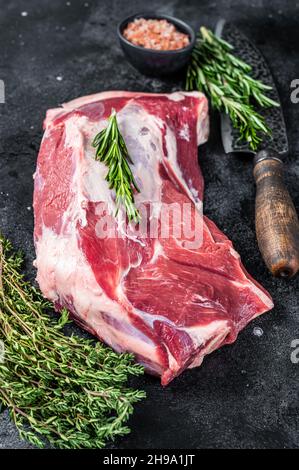 Fresh Raw lamb or goat shoulder meat with butcher knife. Black background. Top view Stock Photo