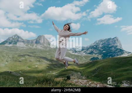 Happy pretty girl jumping high in the mountains. Young women joyfully jumping with mountain in background Stock Photo