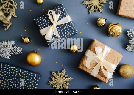 Christmas flat lay composition. Elegant Christmas gift boxes with golden baubles and snowflakes decorations on dark blue background. Stock Photo