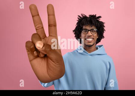 Cool African American teen guy showing big peace or victory gesture over pink studio background Stock Photo