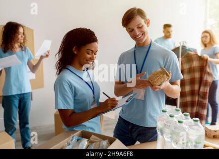 African american female activist checking charity list, working with volunteers, making food packages for people in need Stock Photo