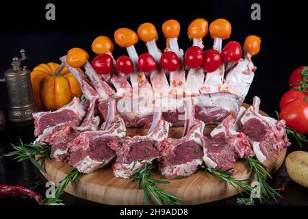 Raw fresh rack of lamb with green herbs. Racks of lamb ready for cooking on dark background. Raw ribs with a rosemary and vegetables. Stock Photo