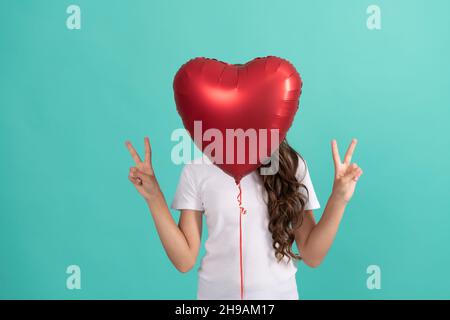 teen girl hiding behind red heart party balloon for valentines day love symbol peace geature, peace Stock Photo