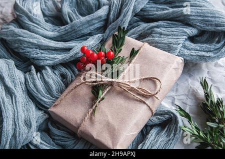 Gift box next to vintage tablecloth gray and spruce leaves with red berries on a black background Stock Photo