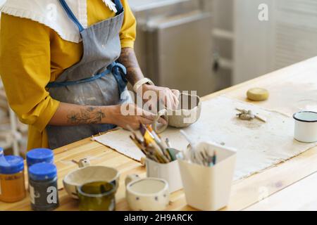 Woman in apron shaping pottery in art studio, making clay mug during ceramics masterclass Stock Photo