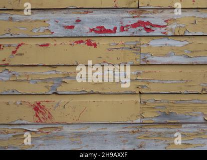 Weathered wood boards on a building exterior with chipped and peeling yellow and red paint. Stock Photo