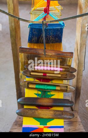 Loom and spools of threads to weave Kente cloth, a type of silk and cotton fabric made of interwoven cloth strips made and native to the Akan ethnic g Stock Photo