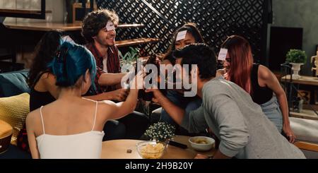 Diverse group of young people partying and toasting a drink in the house enjoying nightlife. Multiethnic friendship and social gathering concept. Stock Photo