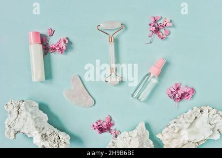 Gua Sha massager and roller from rose quartz, face serum and cream on blue background. Flat lay. Stock Photo