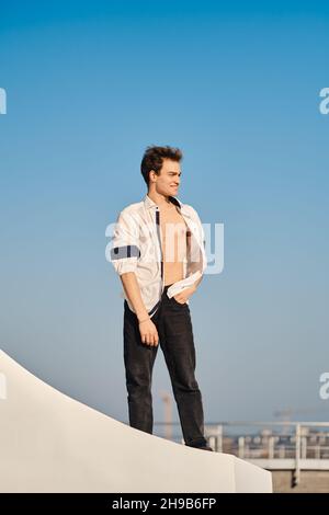 Full length portrait of a young man in unfastened white shirt on the street Stock Photo