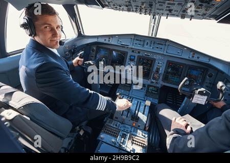 Satisfied pilot in command of airplane operating power lever and looking at camera Stock Photo