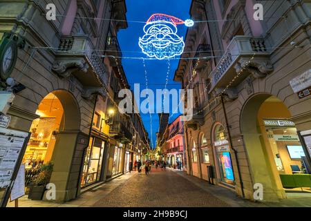 Pedestrian cobblestone street among historic buildings illuminated with Christmas lights in old town of Alba, Italy. Stock Photo