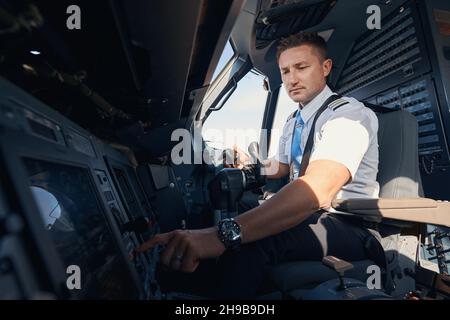 Sideway photo of Caucasian second pilot in uniform pushing control panel button on dashboard Stock Photo