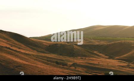Aerial view of exciting red hills covered with shrubs and large green farmlands against the evening sky in summer day. Amazing colorful landscape Stock Photo