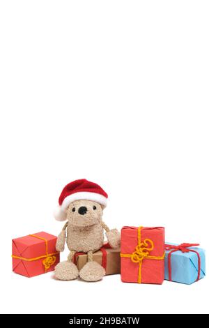 Small teddy bear in a Santa Claus hat sits on boxes with Christmas gifts.On a white background Stock Photo