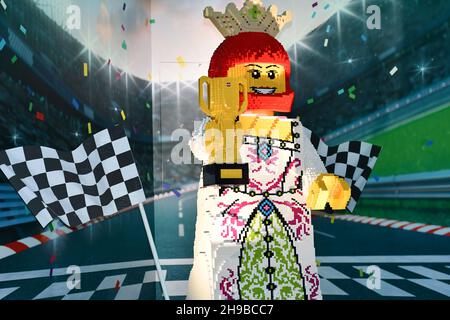 A Lego figure made out of Lego blocks of a racing car driver with a winners trophy with the backdrop of a racing circuit Stock Photo