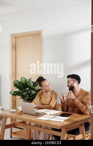 Serious colleagues sitting at office desk and discussing project details and strategy of development at meeting Stock Photo